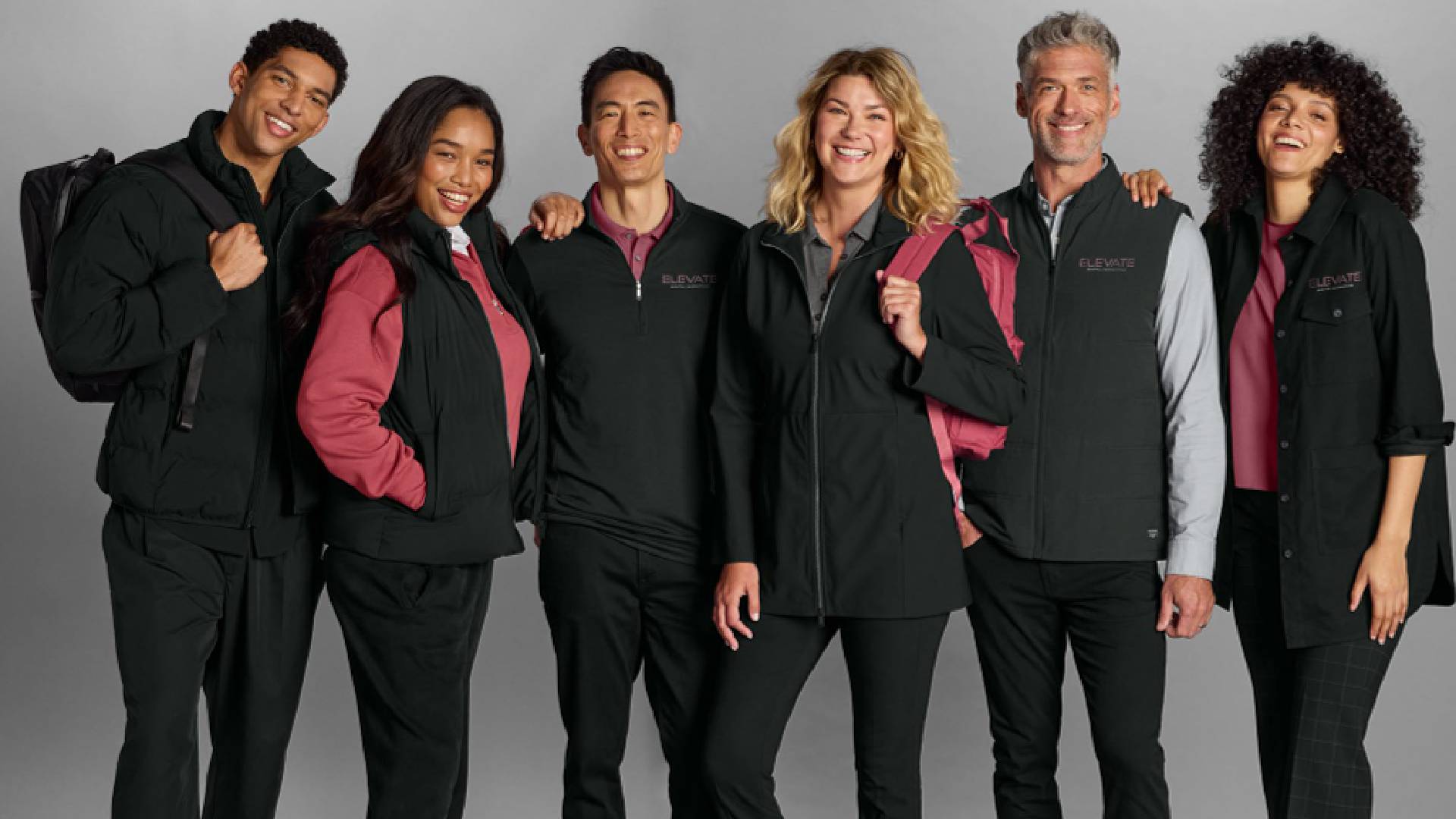 Group of six diverse professionals wearing coordinated branded black and burgundy workwear, including jackets, vests, and polos, showcasing a polished uniform program. by Feury Image Group