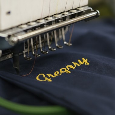 Embroidery machine stitching a personalized employee name onto navy workwear fabric for a custom uniform program.