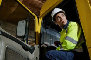 Transportation worker wearing high-visibility safety apparel and hard hat seated in a commercial vehicle cab