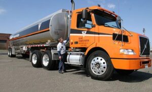 Fuel transport driver standing beside tanker truck wearing transportation workwear and safety apparel