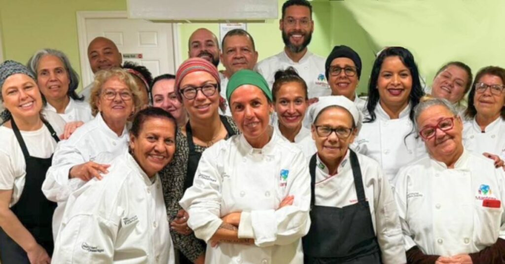 Chef Morena Leite and participants wearing custom embroidered chef coats during a culinary education workshop hosted by Mantena Global Care and supported by Work Hard Dress Right in Newark, New Jersey.